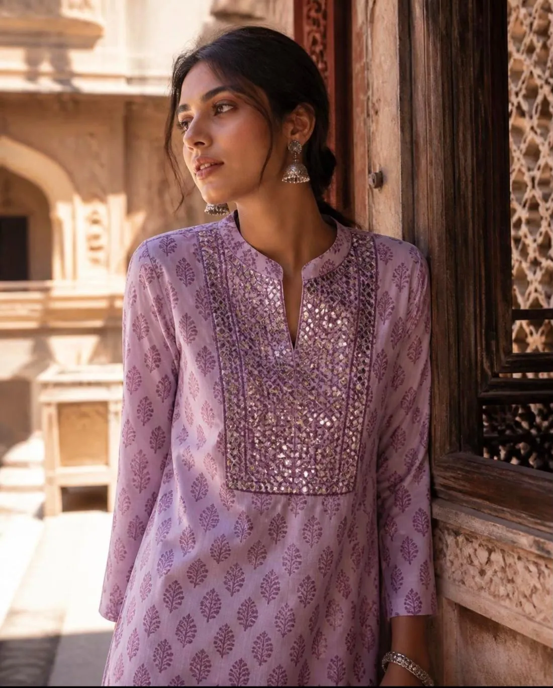 Woman in a lavender block-printed cotton kurti with mirror-work yoke by a carved haveli window